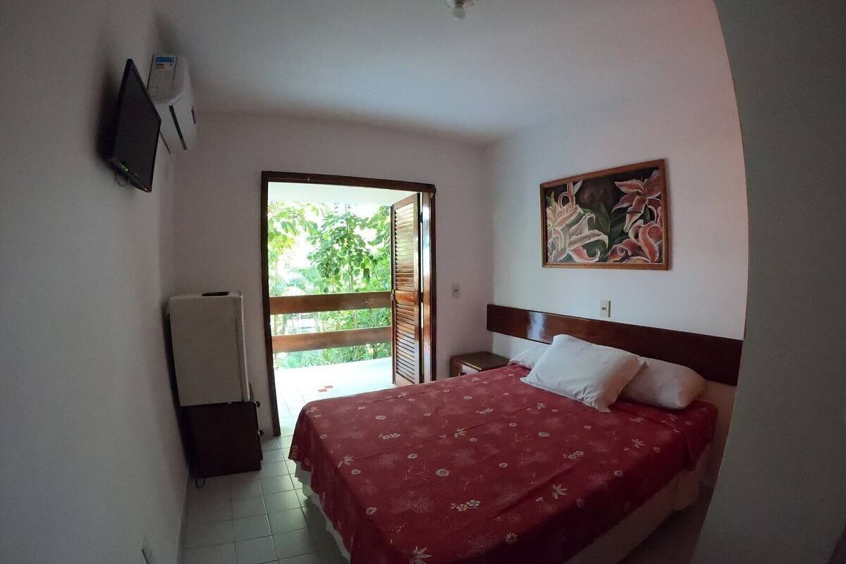 A bedroom with a bed, a painting, a television, and a door leading to an outdoor area.