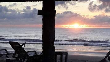 A beach view with a sunset, a wooden deck, and lounge chairs.
