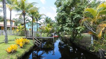 A serene waterway with a wooden bridge, surrounded by lush greenery and palm trees.