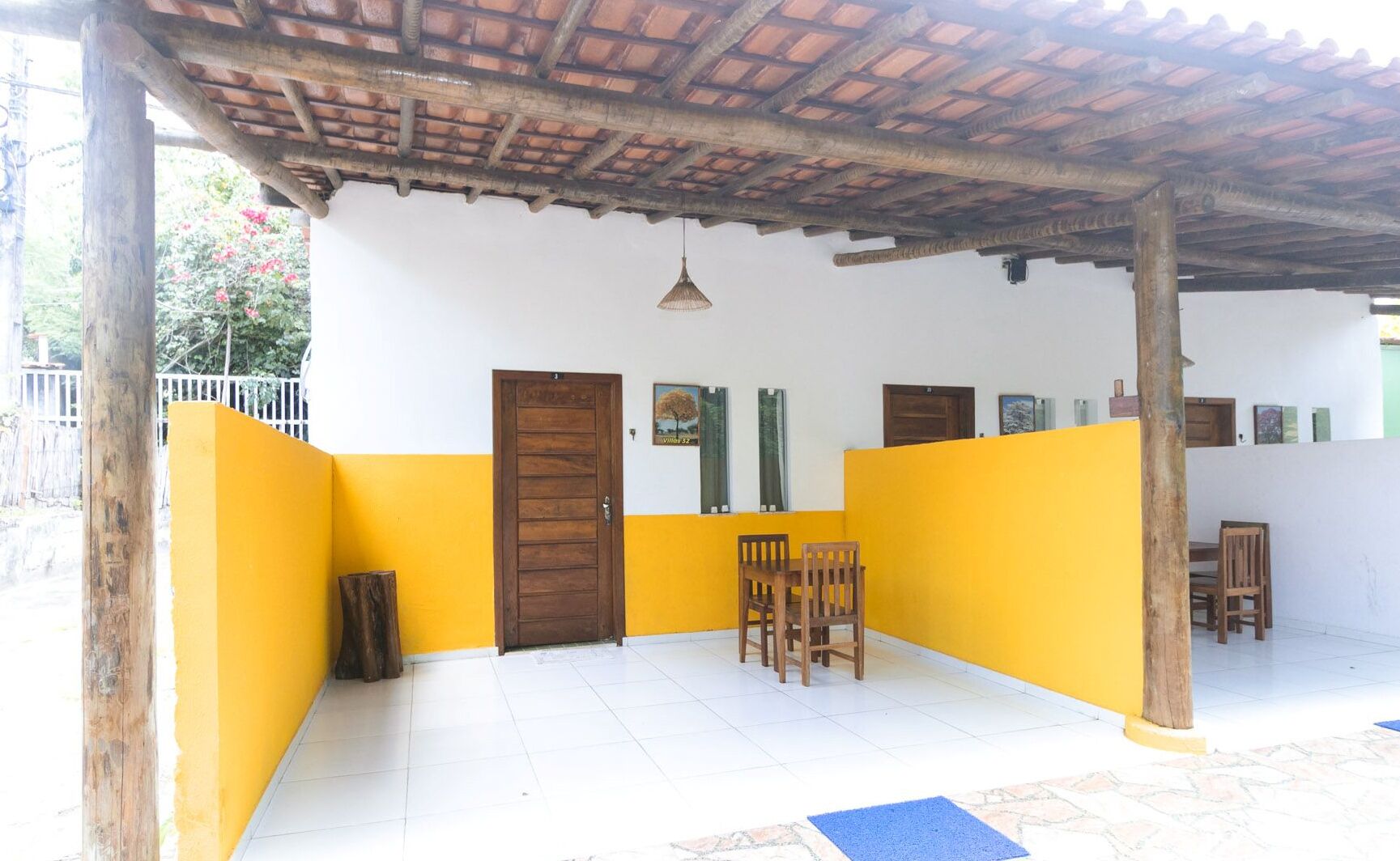 A covered patio area with a tiled floor, a wooden door, and two wooden chairs.