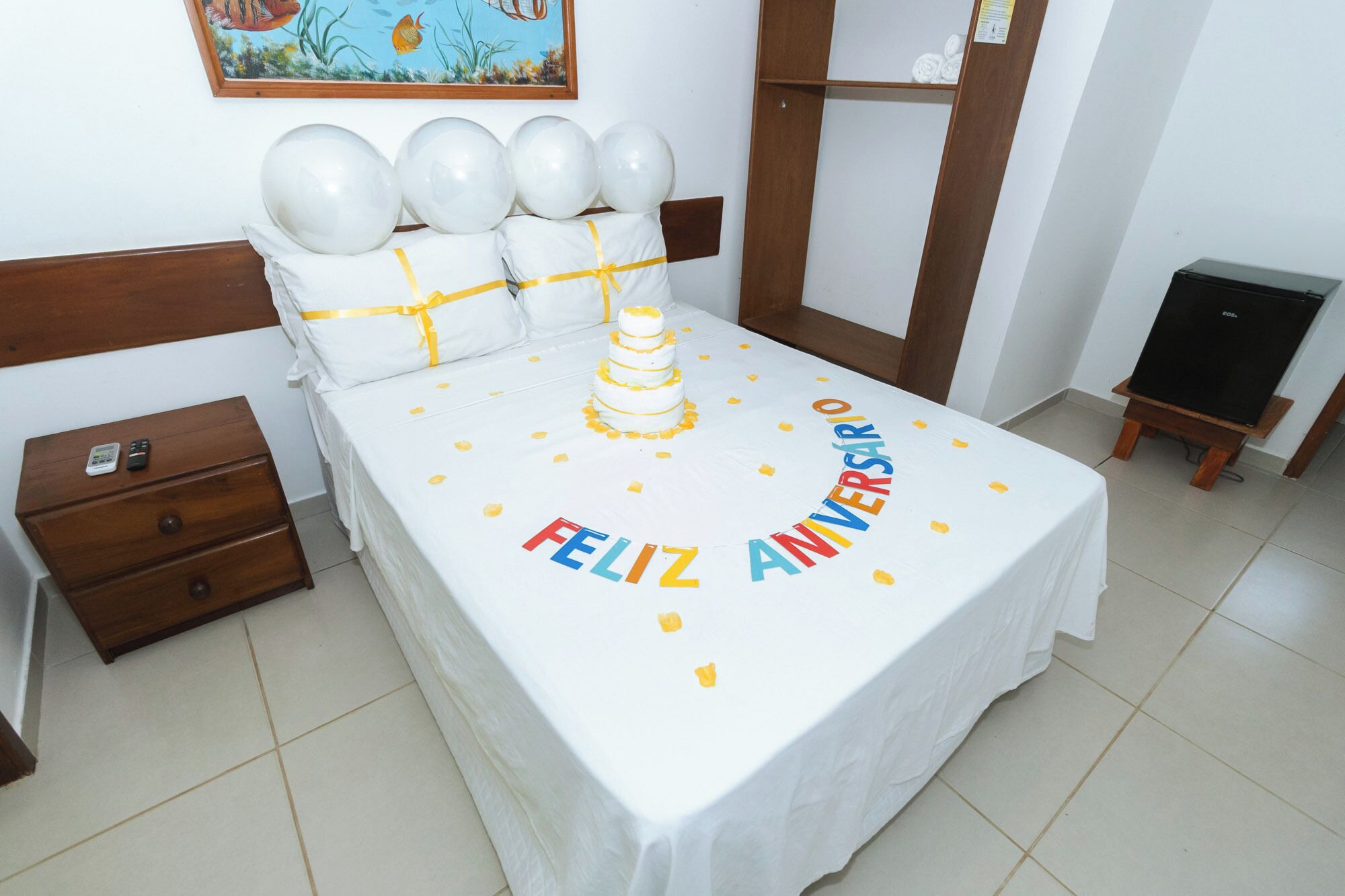 A bed with a white bedspread, a birthday cake, and balloons.