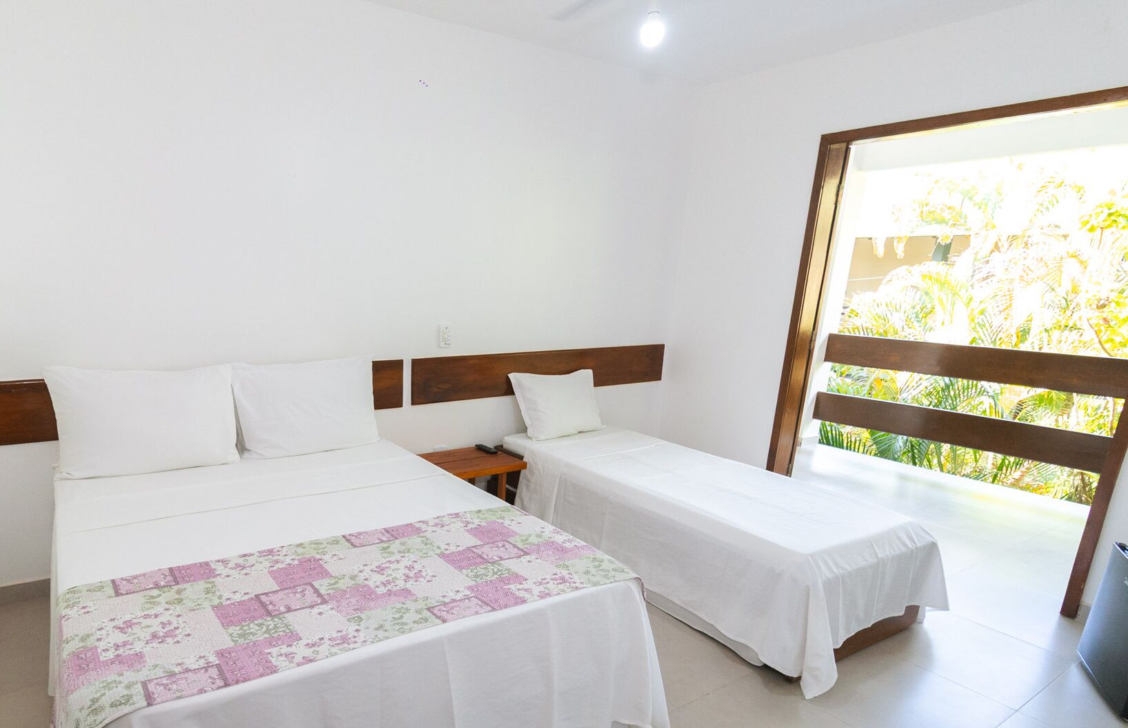 Habitación de hotel con dos camas individuales, una mesita de noche y una ventana con vistas a zonas verdes.