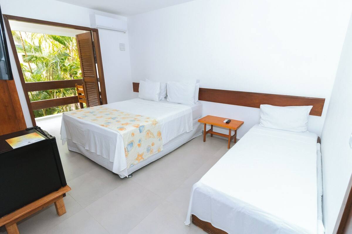 A hotel room with two beds, a wooden nightstand, a TV, and a window with a view of palm trees.