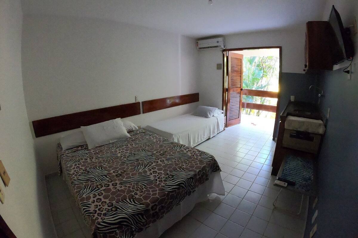 A bedroom with a zebra-patterned bed, a small kitchenette, and a view of greenery through an open door.