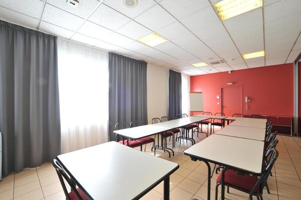 A conference room with tables and chairs, large windows with curtains, a red accent wall, and a ceiling with fluorescent lights. - Brit Hotel Moulin de la Pioline (Aix-en-Provence)
