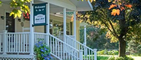 A covered porch with a "Welcome to Oak Hill" sign, white railings, and a staircase leading up to the entrance.