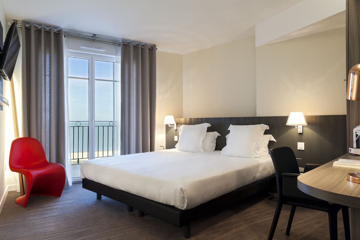 Habitación de hotel con cama, escritorio, silla y balcón.