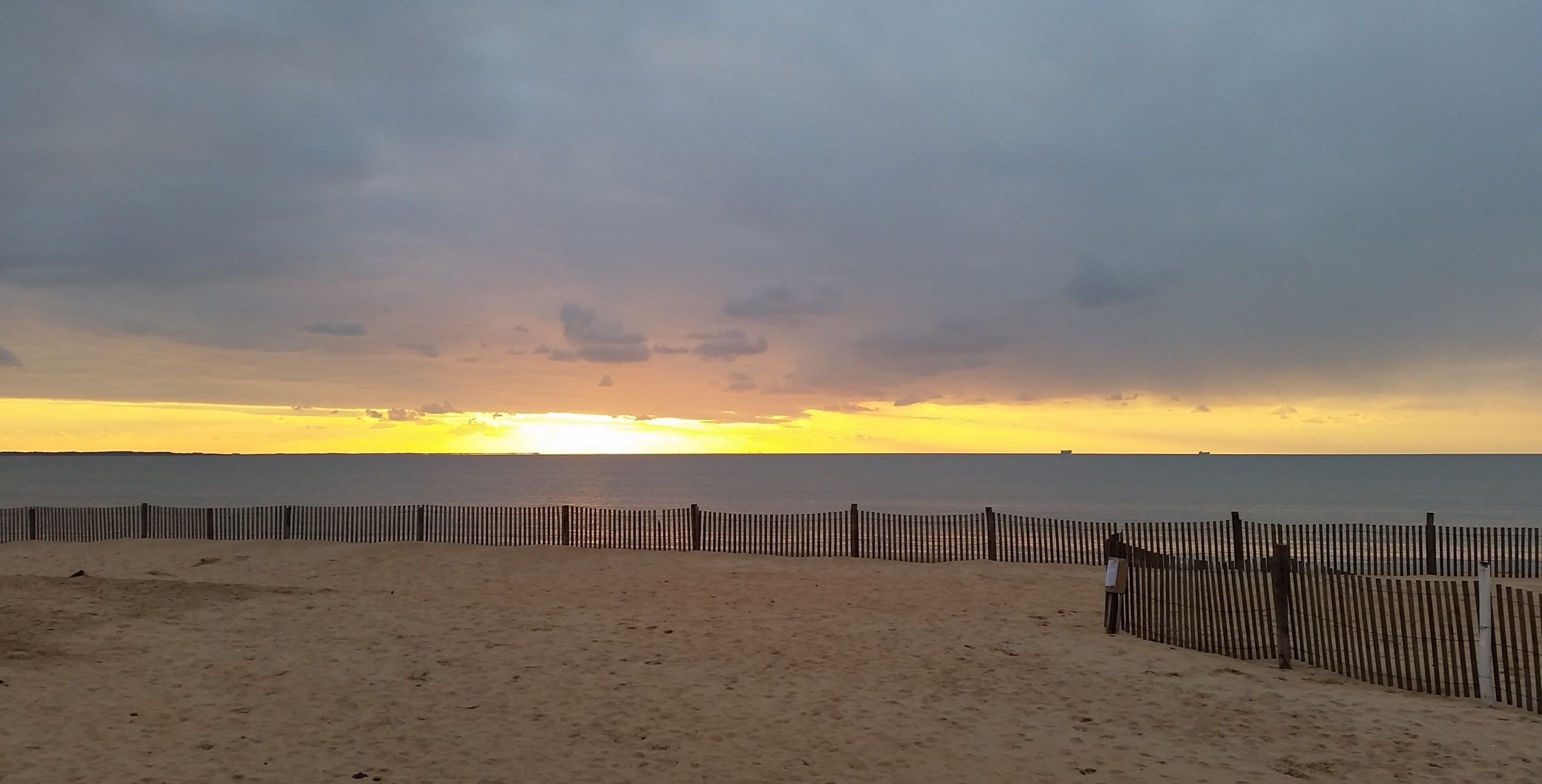 A beach with a wooden fence and a sunset in the background.