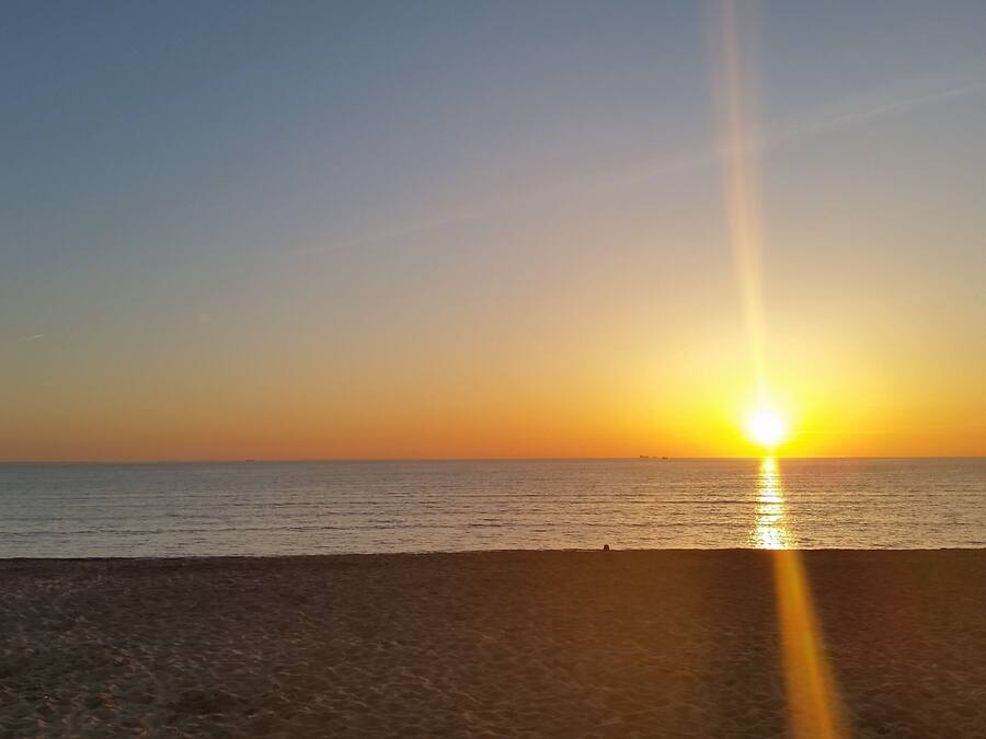 Ein Strand bei Sonnenuntergang, die Sonne tief am Horizont, wobei sich das Licht auf dem Wasser spiegelt.