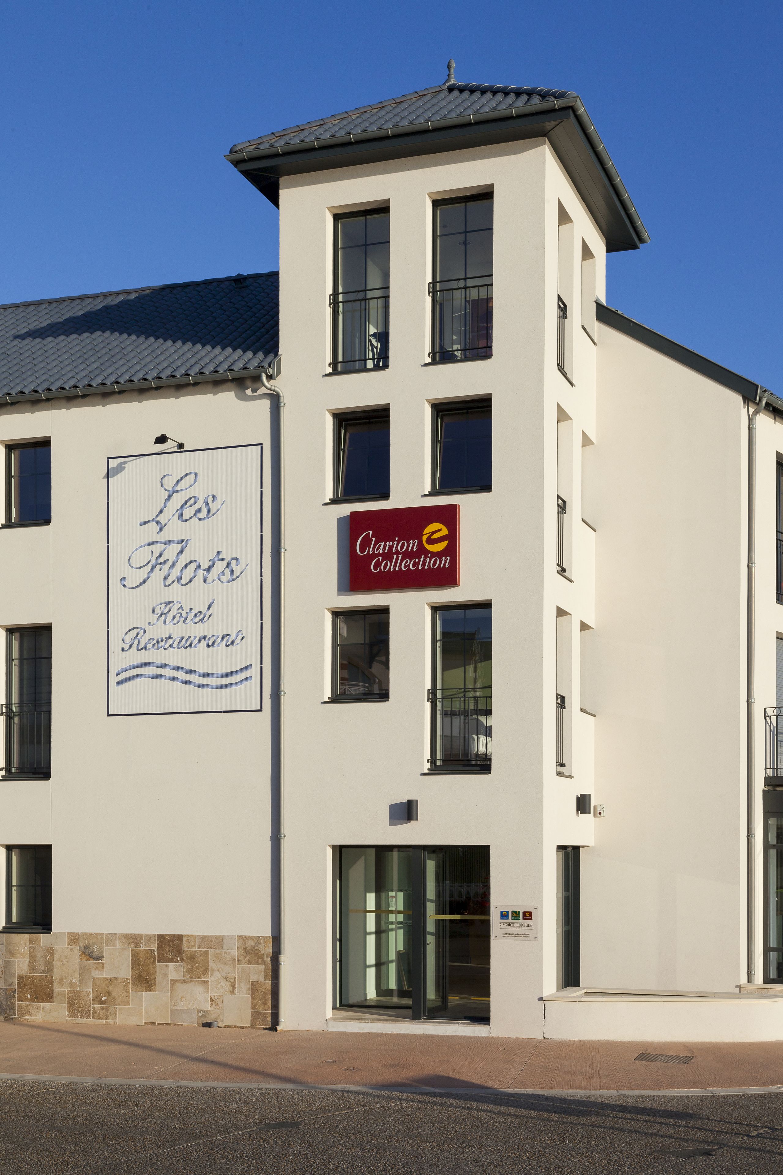 Un hôtel avec une enseigne indiquant « Les Flots, hôtel-restaurant » et une autre indiquant « Clarion Collection ».