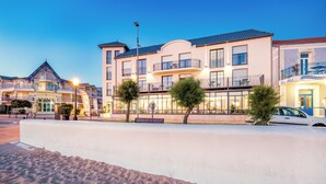 A beachfront hotel with multiple balconies, a sandy beach in the foreground, and a clear sky.