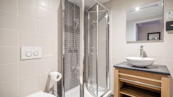 A modern bathroom with a glass-enclosed shower, a white sink, and a wooden vanity.