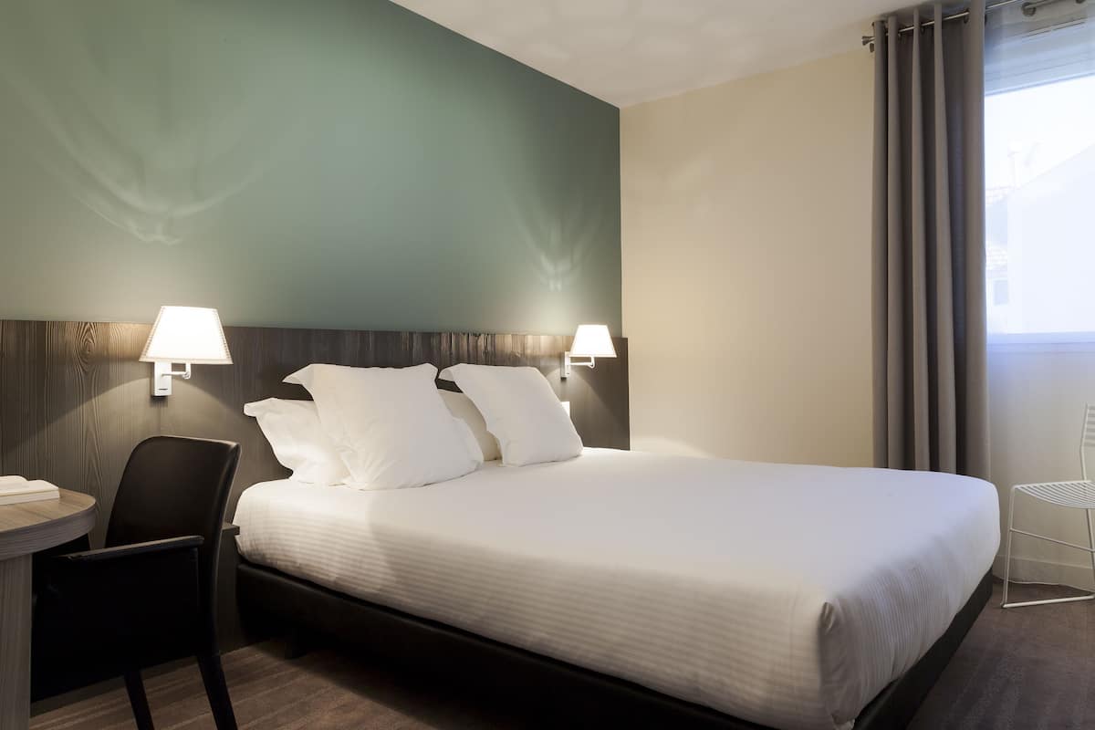 Una habitación de hotel con cama, dos lámparas de noche, una silla y un escritorio.