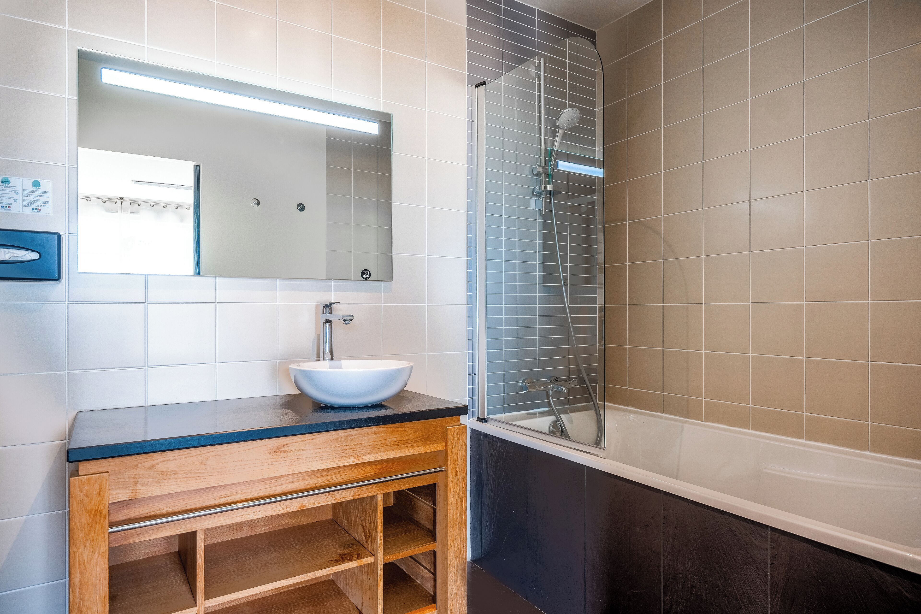 A modern bathroom with a wooden vanity, a white sink, a mirror, and a glass-enclosed shower area.
