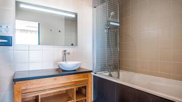 Une salle de bain moderne avec un meuble-lavabo en bois, un lavabo blanc, un miroir et une douche séparée par une paroi de verre.