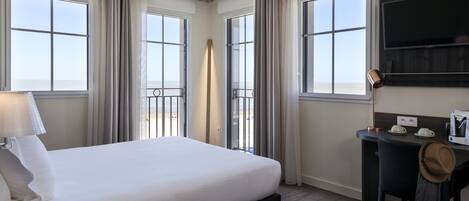Una habitación de hotel con una cama grande, un escritorio, un televisor y un balcón con cortinas.