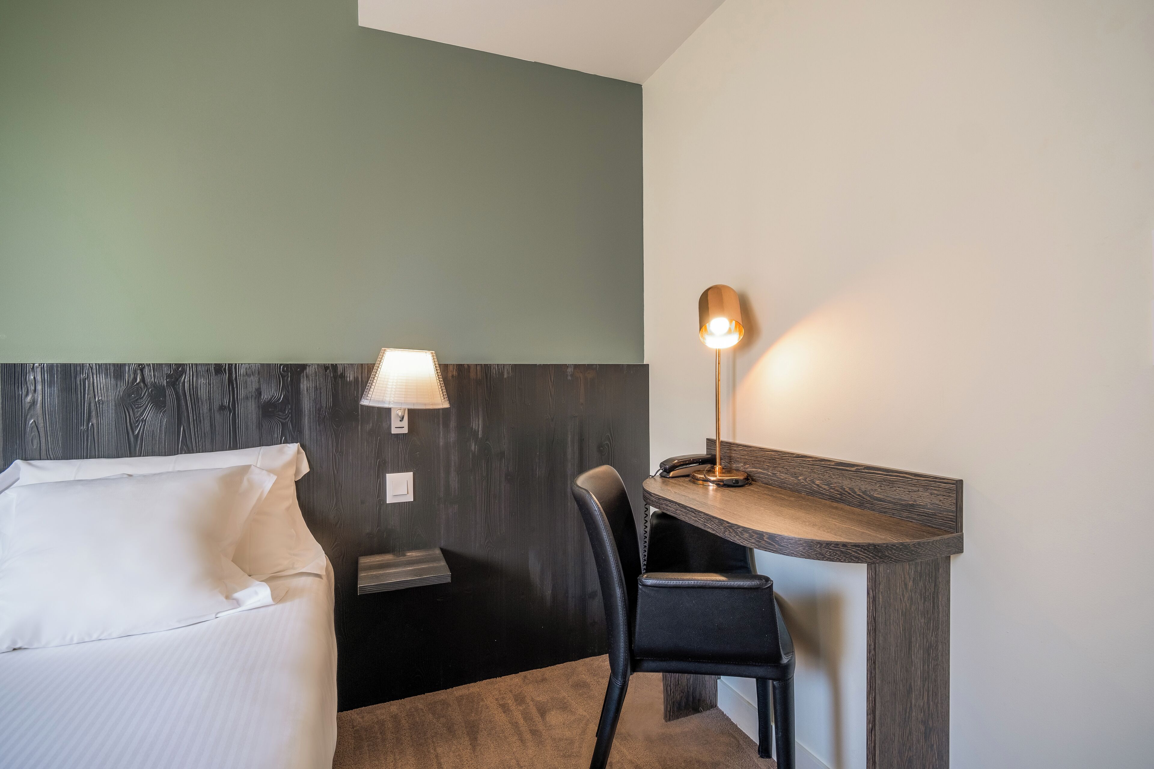 Een hotelkamer met een bed, een bureau, een stoel, een lamp en een wandplank.
