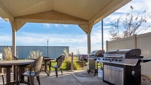 Un patio exterior con una parrilla, sillas y una zona cubierta.