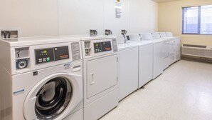 Un lavadero con varias lavadoras y secadoras industriales, paneles de control y sistema de ventilación.