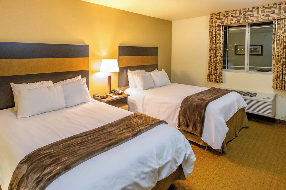 A hotel room with two beds, a nightstand, a lamp, and a window with curtains.