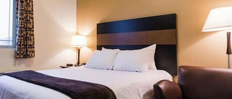 Una camera d'albergo con un letto, un comodino, una lampada, una sedia e una finestra con tende a motivi.