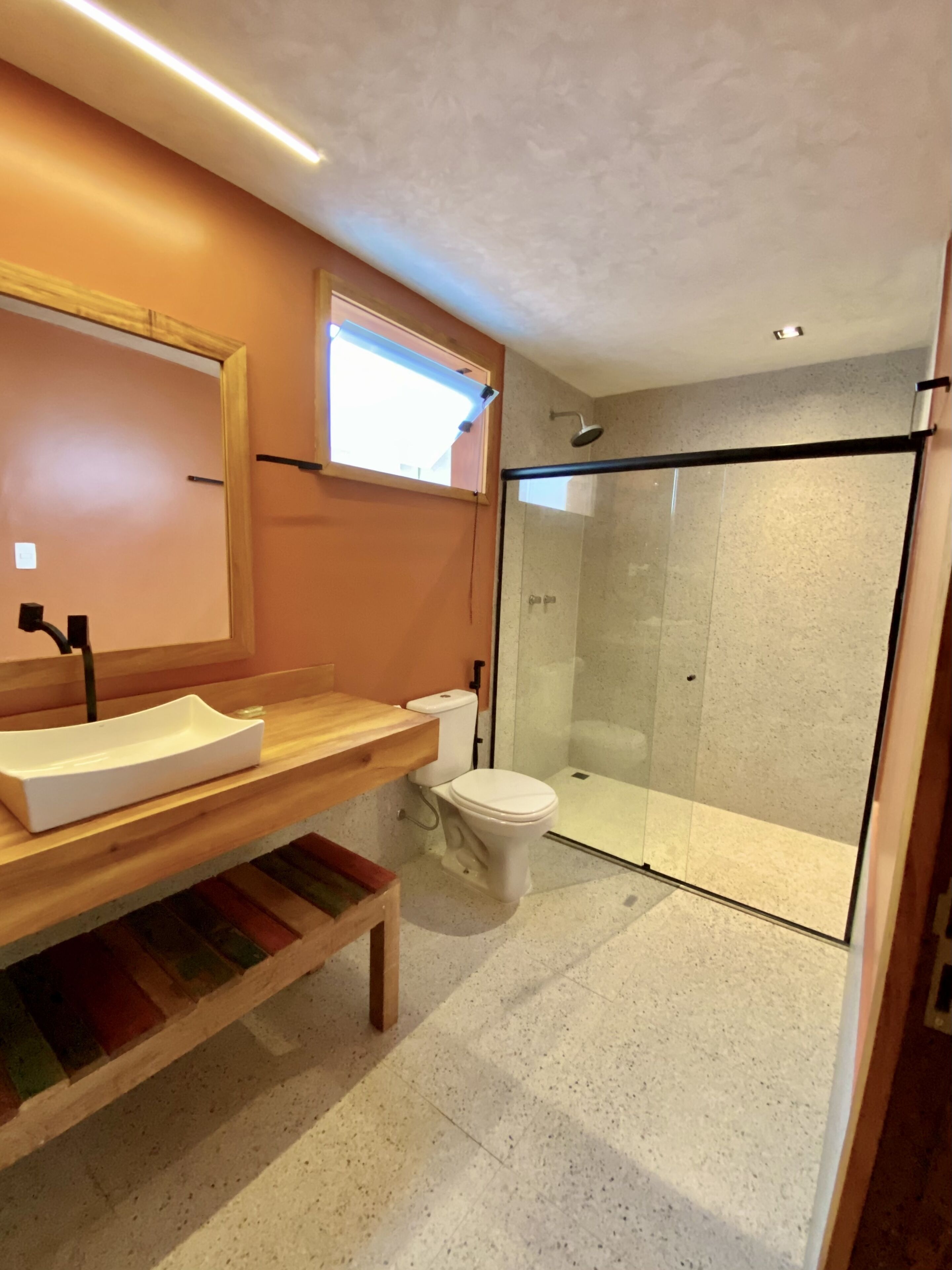 A modern bathroom with a wooden vanity, a white toilet, and a glass-enclosed shower.