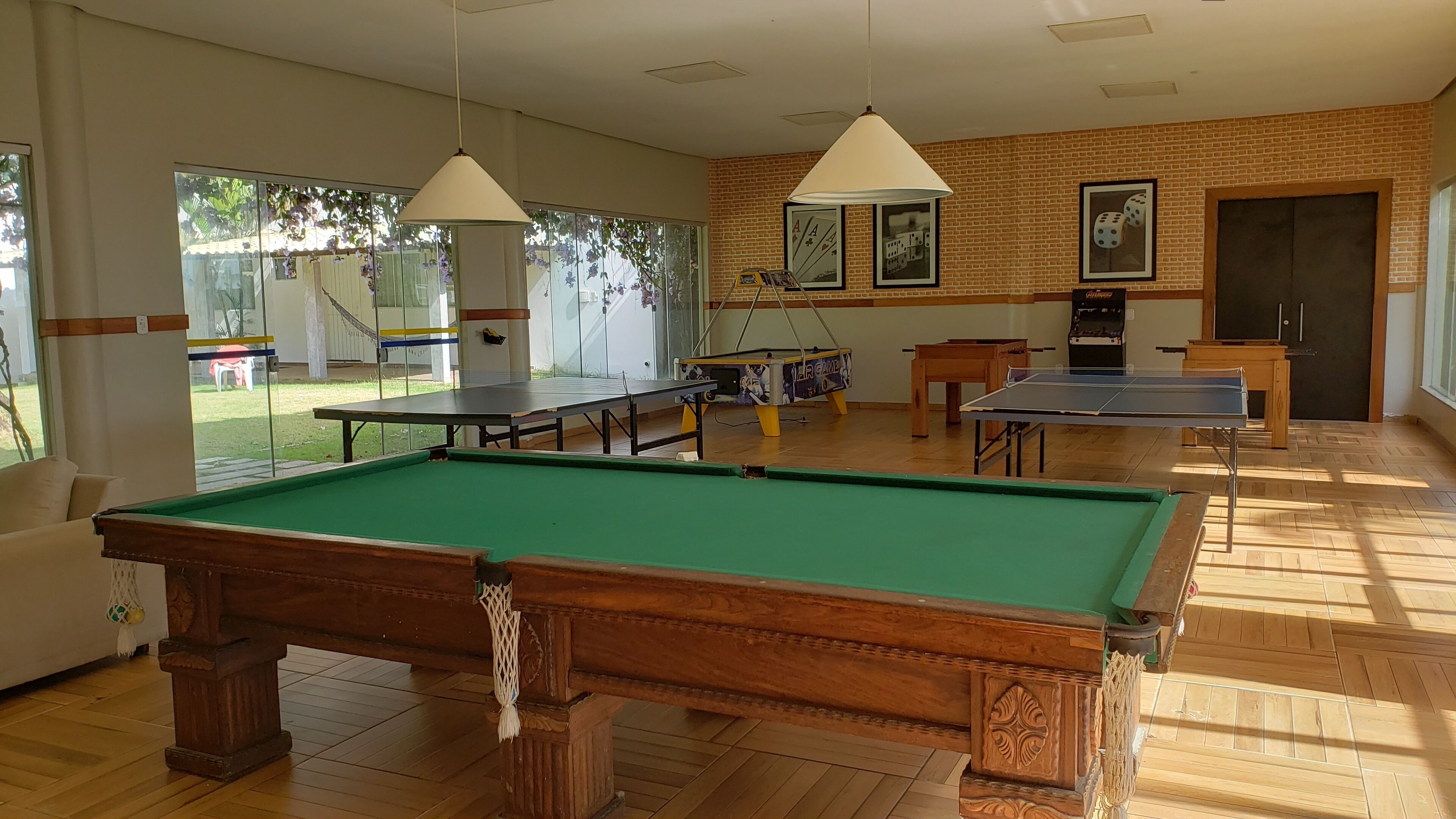 Een pooltafel, twee tafeltennistafels en een tafelvoetbaltafel in een ruimte met bakstenen muren en grote ramen.