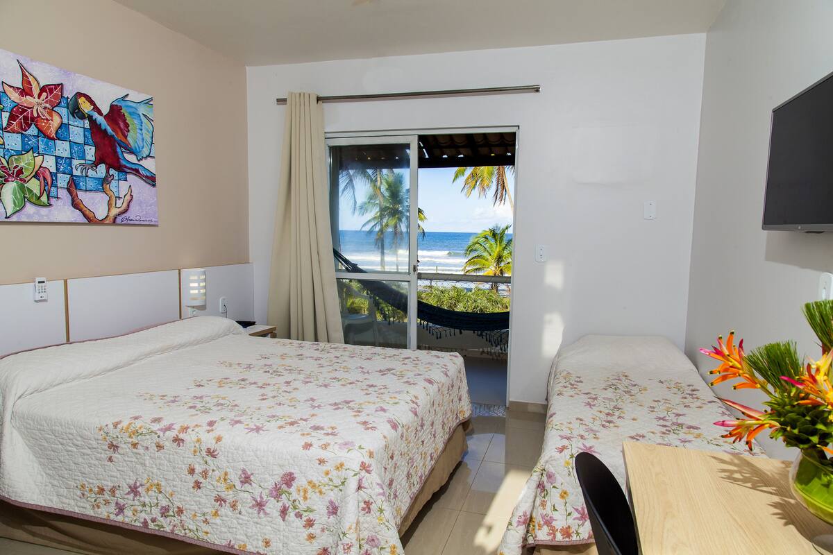 Une chambre d’hôtel avec deux lits, une télévision, un balcon donnant sur l’océan et un tableau au mur.