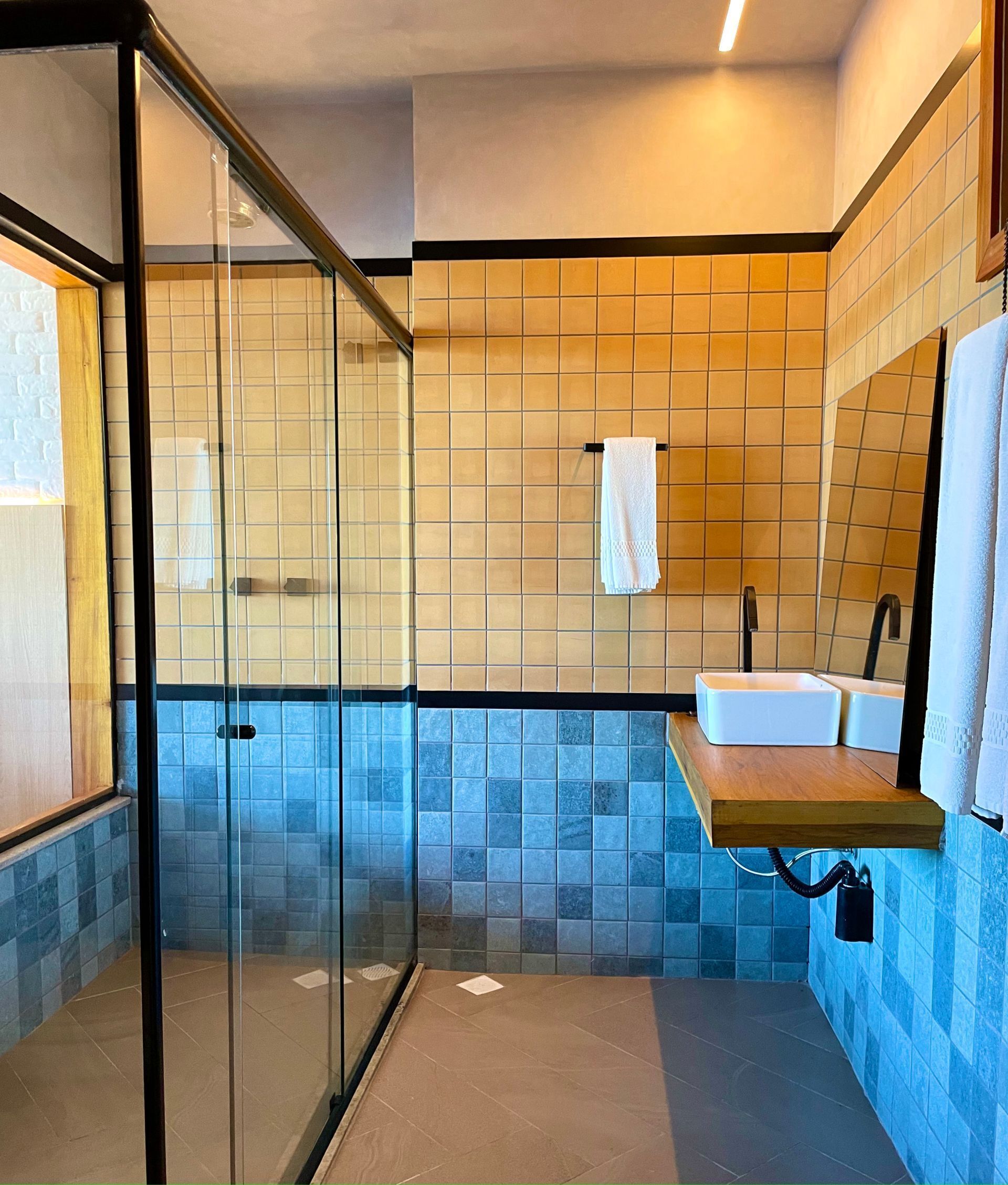 A modern bathroom with a glass shower enclosure, a sink with a wooden countertop, and tiled walls in beige and blue.