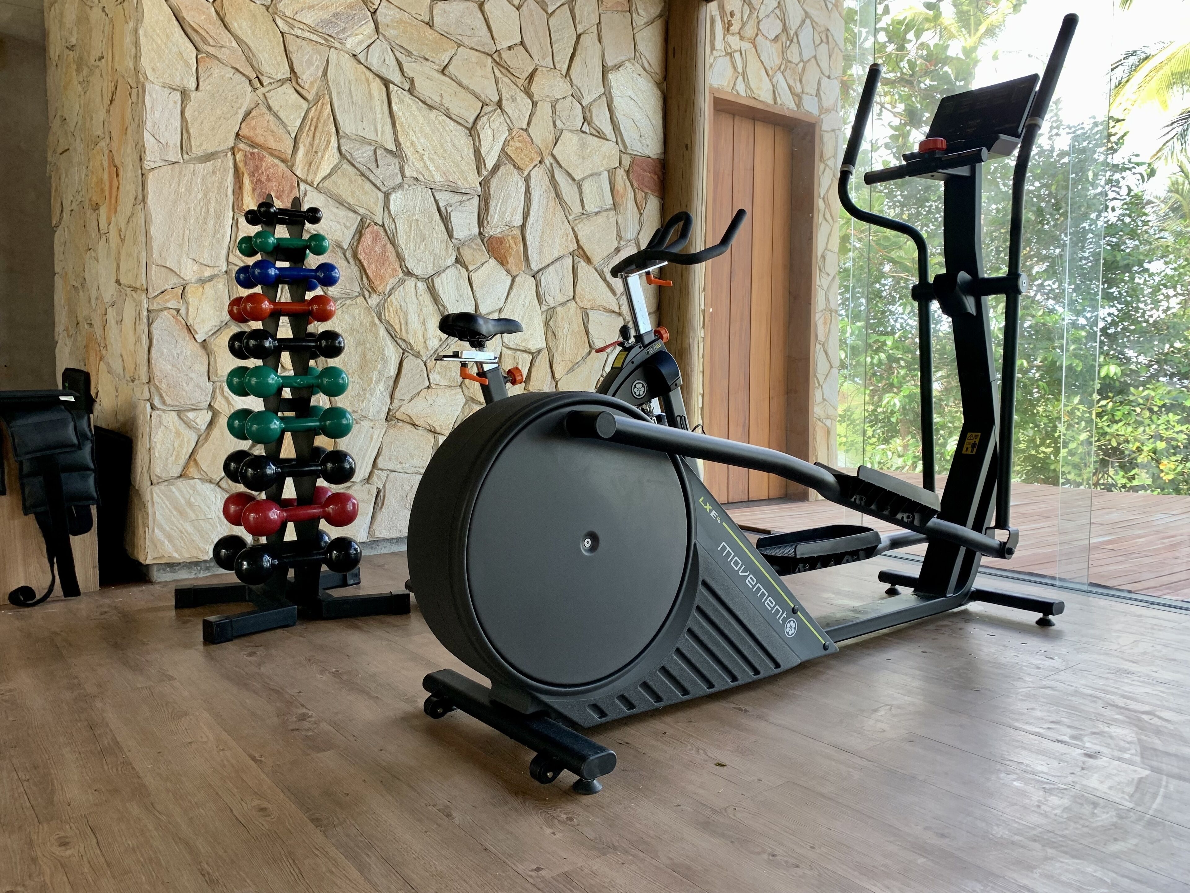 Un espacio de ejercicios con una máquina de remo, una bicicleta estática y un soporte de mancuernas en la pared.
