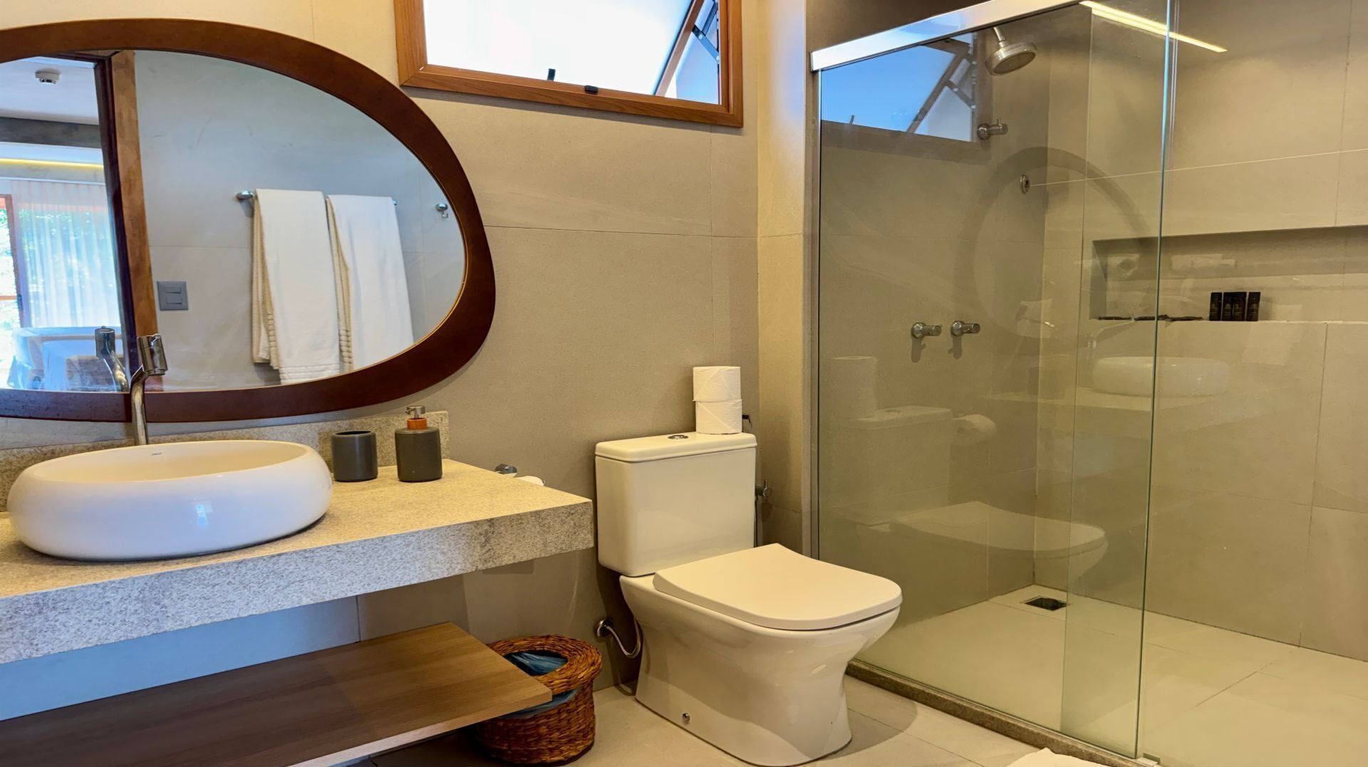 Un baño moderno con un espejo redondo, un lavamanos, un inodoro y una ducha con mampara de vidrio.