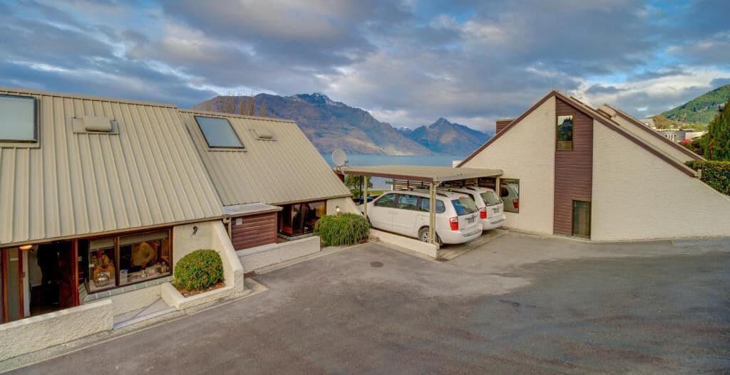 A hotel with a parking area, two buildings with sloped roofs, and a mountainous backdrop.