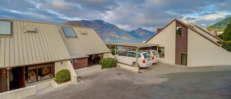 A hotel with a parking area, two buildings with sloped roofs, and a mountainous backdrop.