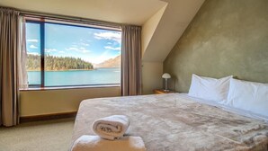 Un dormitorio con una cama grande, vistas a un lago y una montaña al fondo.