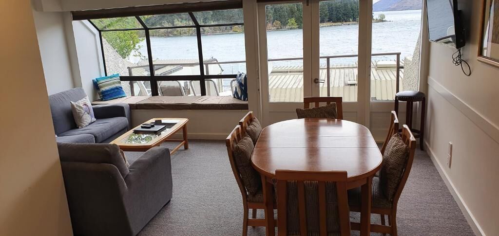 Une pièce comprenant un canapé, une table basse, une table à manger avec des chaises, et offrant une vue sur un lac grâce à de grandes fenêtres.