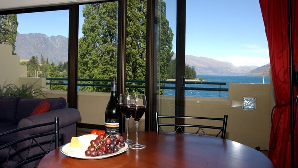 A dining area with a table set for two, a bottle of wine, and a plate of grapes and cheese. - Lakefront Apartments (Queenstown)