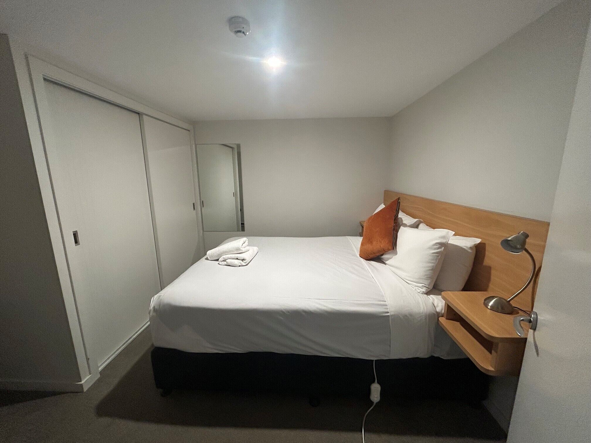 Una habitación de hotel con una cama individual, una mesita de noche, una lámpara y un enchufe.