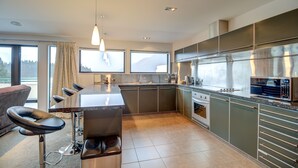 Una cocina moderna con una isla central, electrodomésticos de acero inoxidable y ventanas amplias con vistas al exterior.