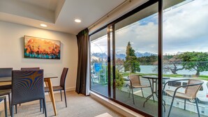 Quarto de hotel moderno com uma grande porta de correr de vidro que dá para uma varanda com vista para um lago e montanhas.
