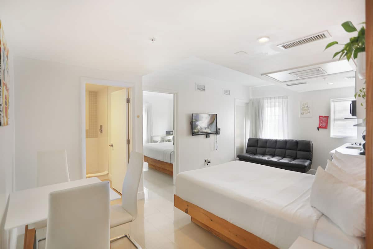 A modern hotel room with a large bed, a seating area, a desk, and a television.