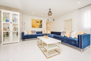 A modern living room with a sectional sofa, a white coffee table, and a glass cabinet with bottles. - Hotel Belleza (Miami Beach)