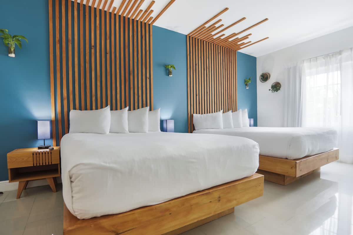 A modern bedroom with two beds, wooden headboards, and a blue accent wall.
