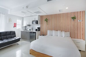A modern hotel room with a large bed, a sofa, a kitchenette, and a striped wall. - Hotel Belleza (Miami Beach)