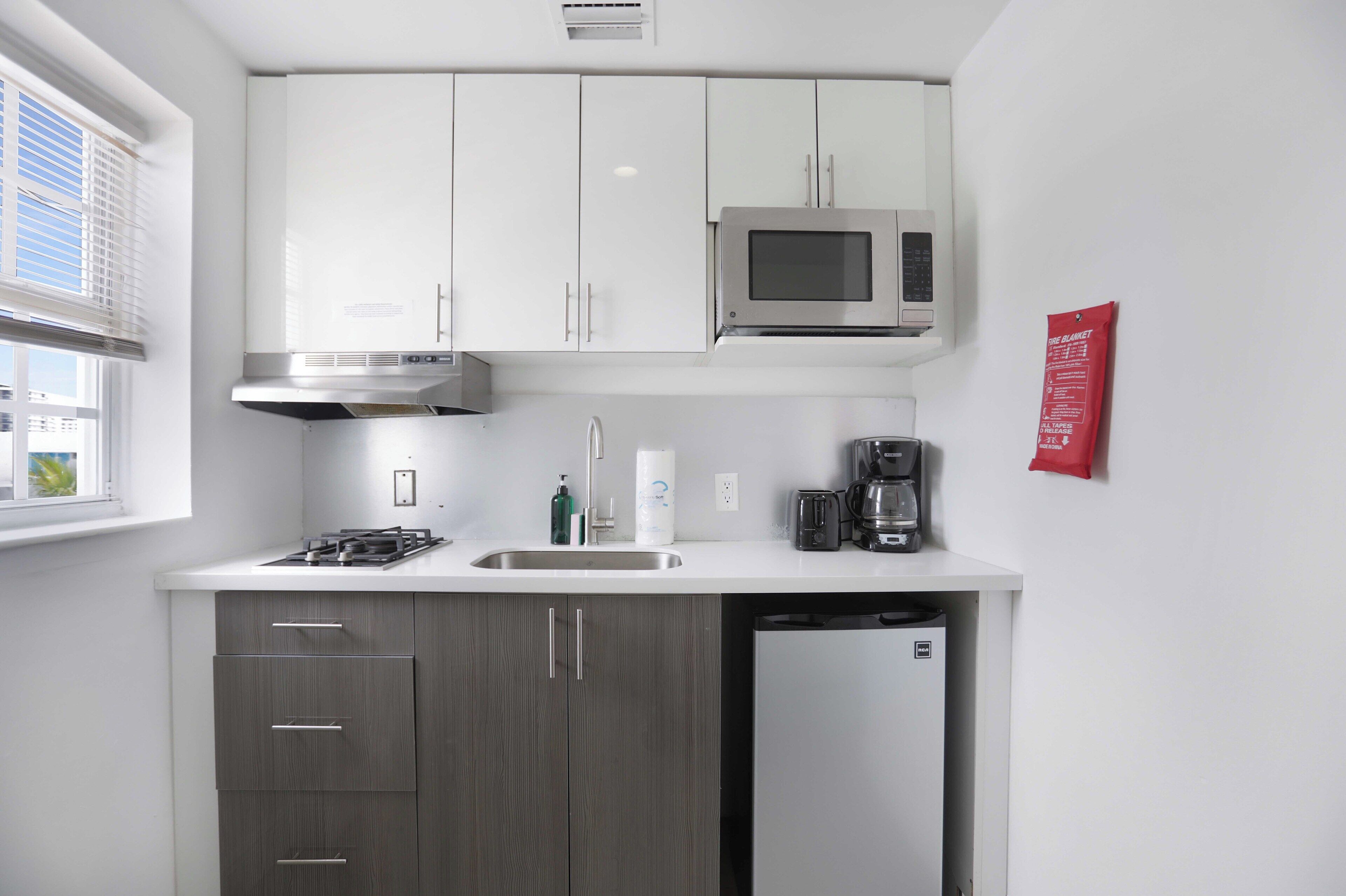 Una cocina moderna con armarios blancos, un microondas de acero inoxidable, una estufa a gas, una cafetera y un lavavajillas.