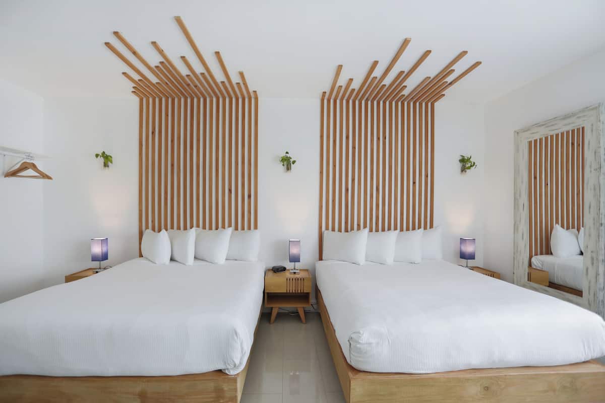 A modern hotel room with two beds, wooden headboards, bedside tables with lamps, and a small plant on each nightstand.