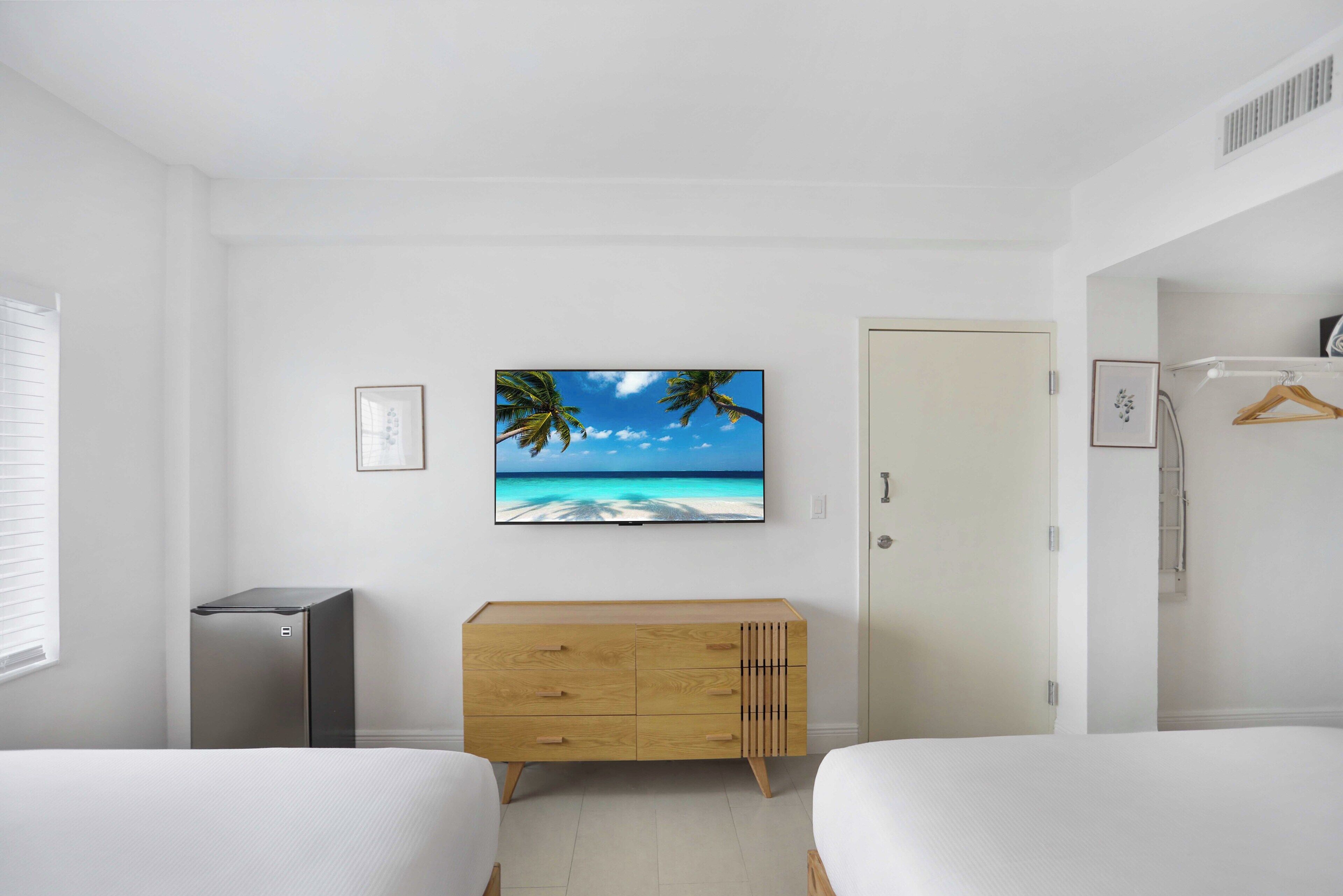 A bedroom with two beds, a wooden dresser, a television on the wall, and a door.