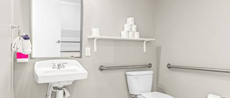 A bathroom with a white sink, toilet, and a mirror. There are two towel racks and a shelf with toilet paper.