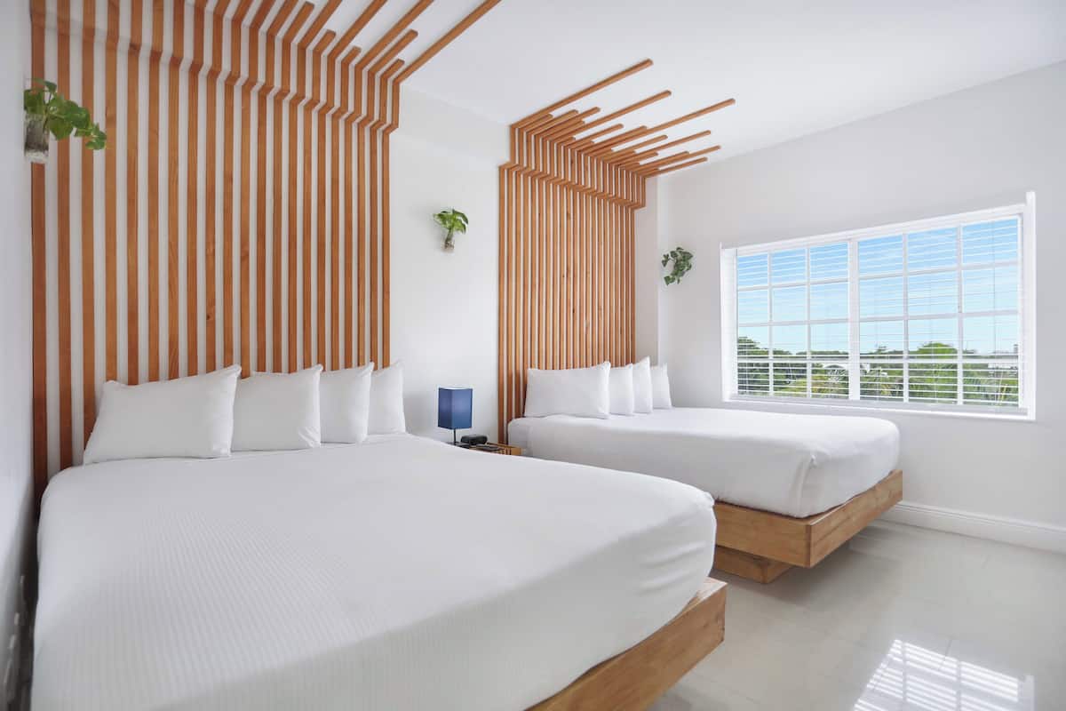 A modern hotel room with two beds, a large window, and a striped wooden headboard.