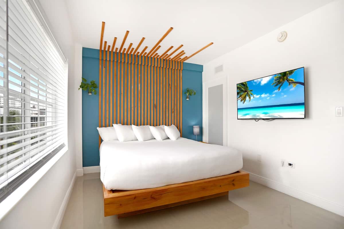 A modern bedroom with a wooden bed frame, a blue accent wall, and a TV displaying a beach scene.