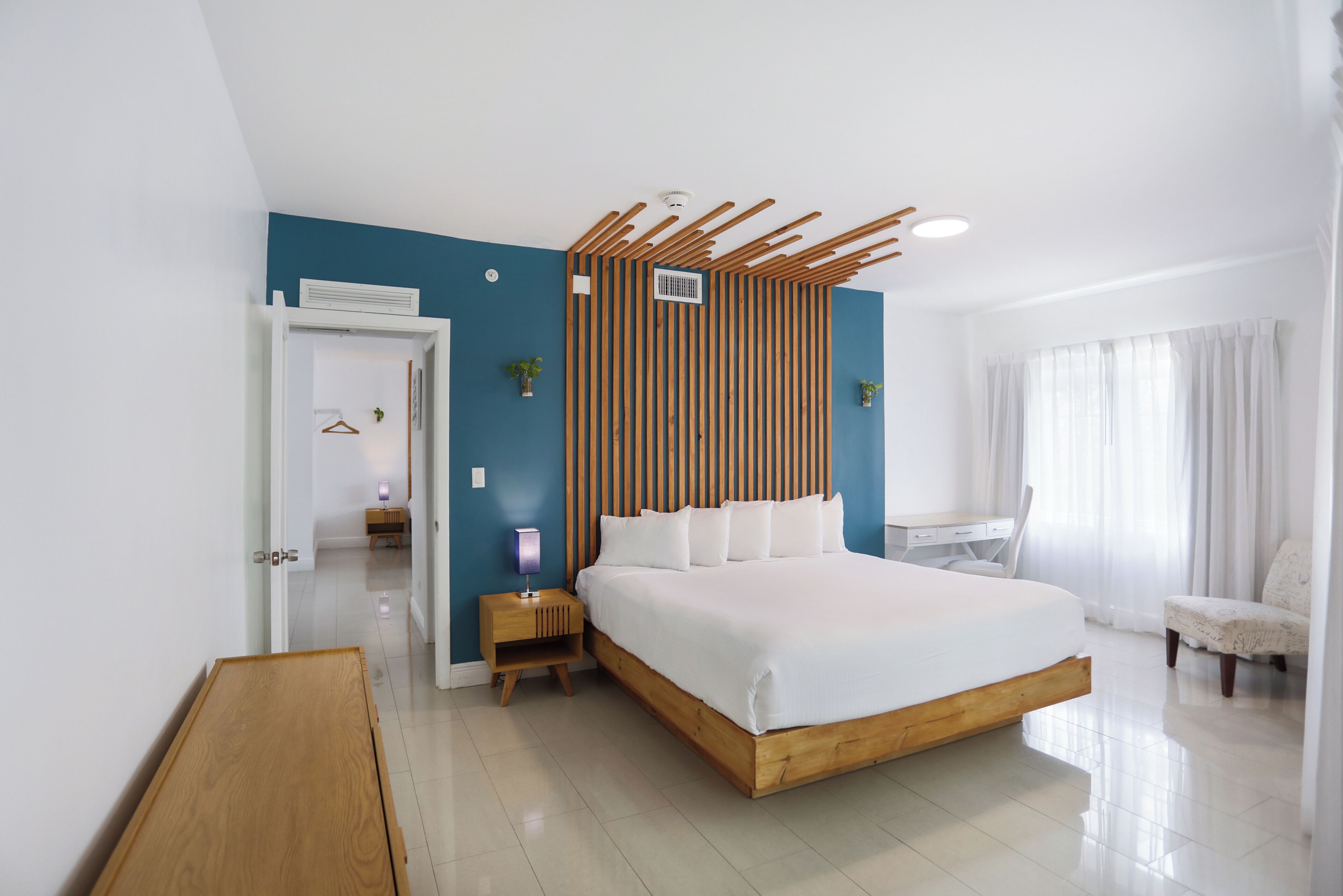 A modern bedroom with a large bed, a wooden headboard, a desk, and a chair.